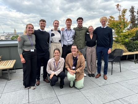 Group of 9 interns stood (and crouched) on the rooftop terrace at The Crown Estate's London office